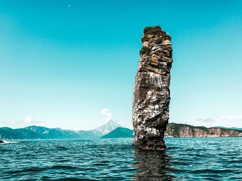 View of rock in sea against clear blue sky