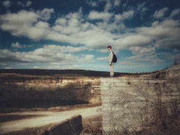 Side view of man standing on abandoned building by lake against cloudy sky