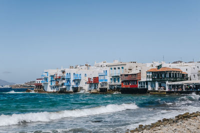 Buildings by sea against clear blue sky