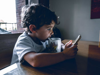 Boy using mobile phone while sitting on laptop