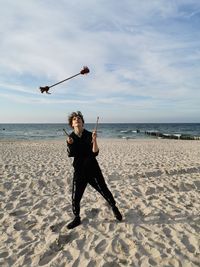 Full length of man on beach against sky, juggling