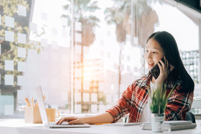 Young woman using mobile phone while sitting on table