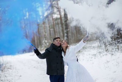 Close-up of couple with distress flare kissing against tree during winter