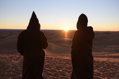 Rear view of silhouette couple standing on beach at sunset