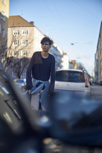 Young woman sitting on car against sky