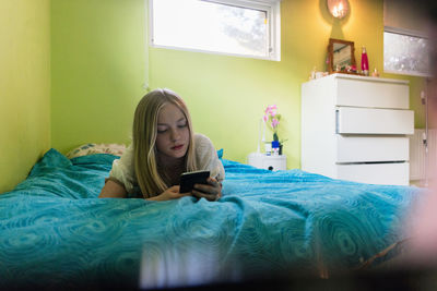 Teenage girl using smart phone while lying on bed at home