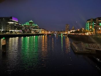 Illuminated buildings by river against sky at night