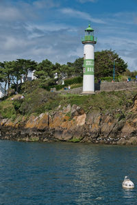 Lighthouse amidst sea and buildings against sky