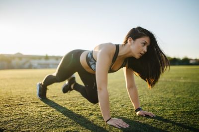 Young woman exercising on grass field against sky