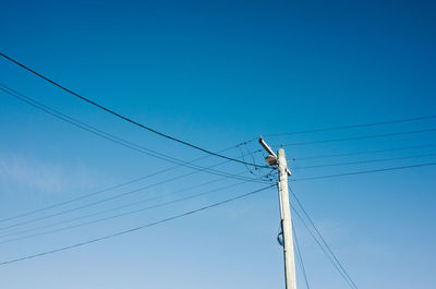 Low angle view of electricity pylon against blue sky