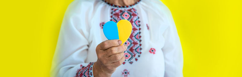 Midsection of woman holding heart shape candy against yellow background