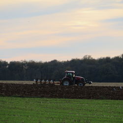 Tractor on field against sky during sunset