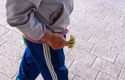 Midsection of man holding flowers while walking on street