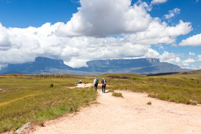 People walking on road amidst field against sky