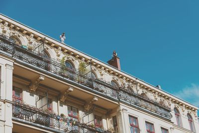 Low angle view of man standing on building terrace against blue sky during sunny day