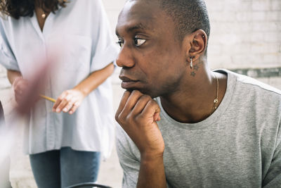 Thoughtful young male hacker looking away while sitting with hand on chin at workplace