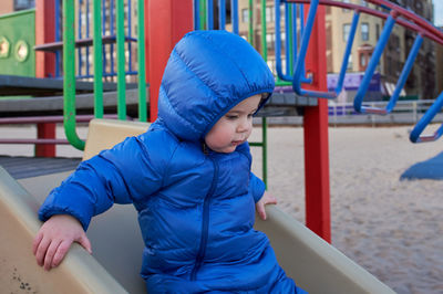 Cute toddler in a winter suit playing at the playground on the beach