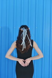 Rear view of woman with long hair standing against blue wall