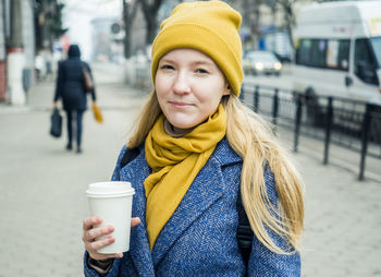 Close-up portrait of woman holding disposable cup while standing in city 