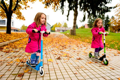 Girls riding push scooters at park during autumn