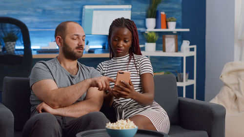 Couple using phone while sitting on sofa by popcorn