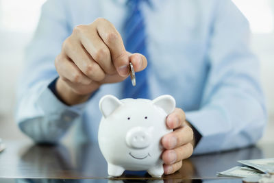 Midsection of businessman putting coin in piggy bank