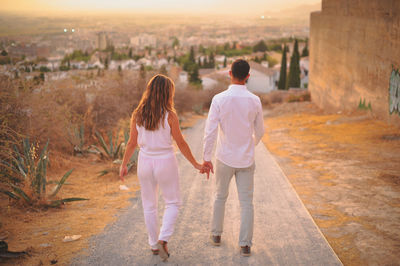 Rear view of young couple walking on road during sunset