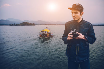 Thoughtful man holding camera while standing river