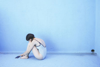 Woman using smart phone in front of blue pool wall