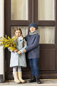 A couple of a boy and a girl of schoolchildren in spring coats with a bouquet of acacia 