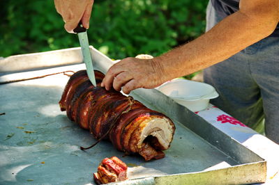 Cropped shot of hands cutting big piece of pork meat on the table in nature