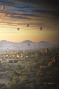 Hot air balloons flying over landscape against sky during sunset