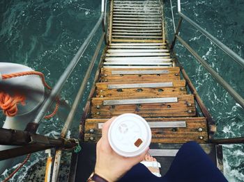 Low section of woman holding coffee on steps over sea