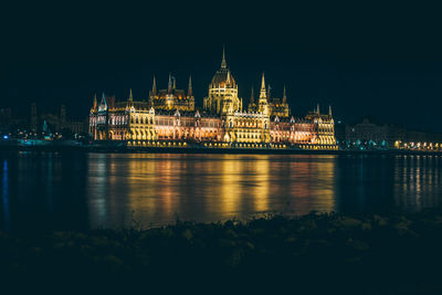 Illuminated hungarian parliament building by river against clear sky at night