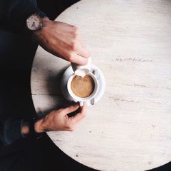 Cropped hands of man pouring milk in coffee on table