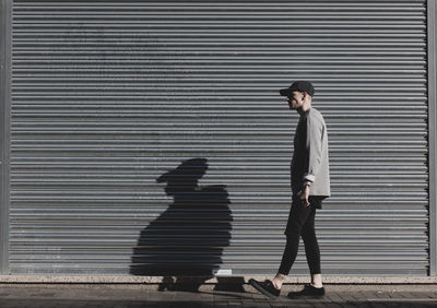 Side view of man walking against closed shutter