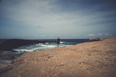 Man standing on rock at beach against sky