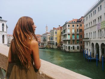 Woman standing by canal in city against sky