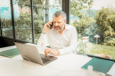 Mature man talking on smart phone while working at home