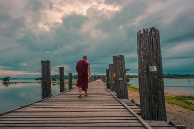 Rear view of monk on pier on sea against sky