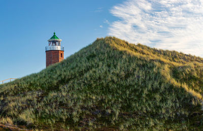 Lighthouse amidst trees and buildings against sky