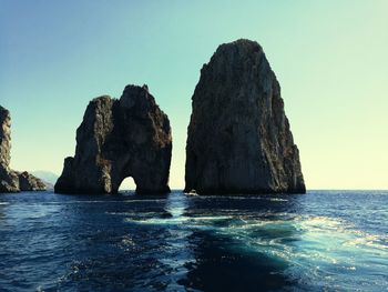 Rock formation in sea against clear sky