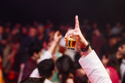 Cropped hand holding beer glass while pointing at music concert