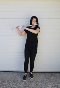 Full length portrait of young woman standing against wall
