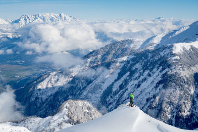 Hiker standing on snowcapped mountain peak while looking at landscape against sky