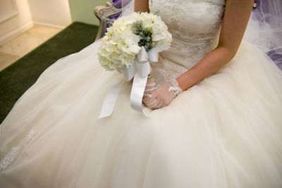 Midsection of bride holding bouquet while sitting on chair