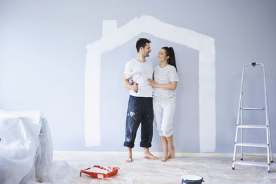 Happy couple painting in new apartment with house shape on wall