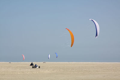 People paragliding over beach against clear sky
