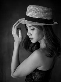 Portrait of young woman wearing hat against black background