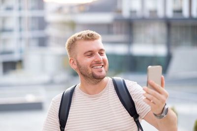 Handsome adult middle-aged blond bearded man, casual clothing, taking selfie in city outdoors